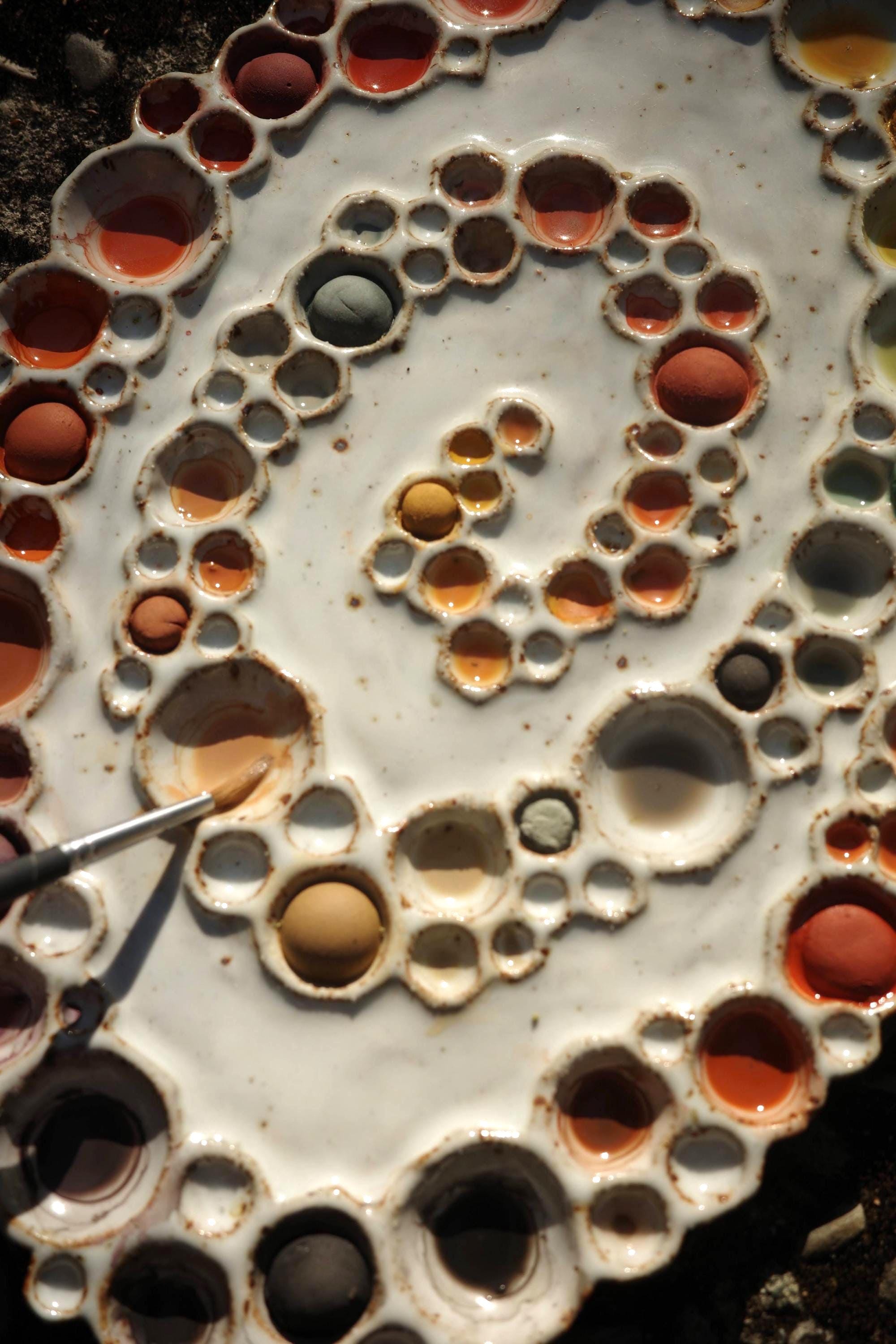 Close-up of large ceramic spiral bubble palette with paints and paint brush 