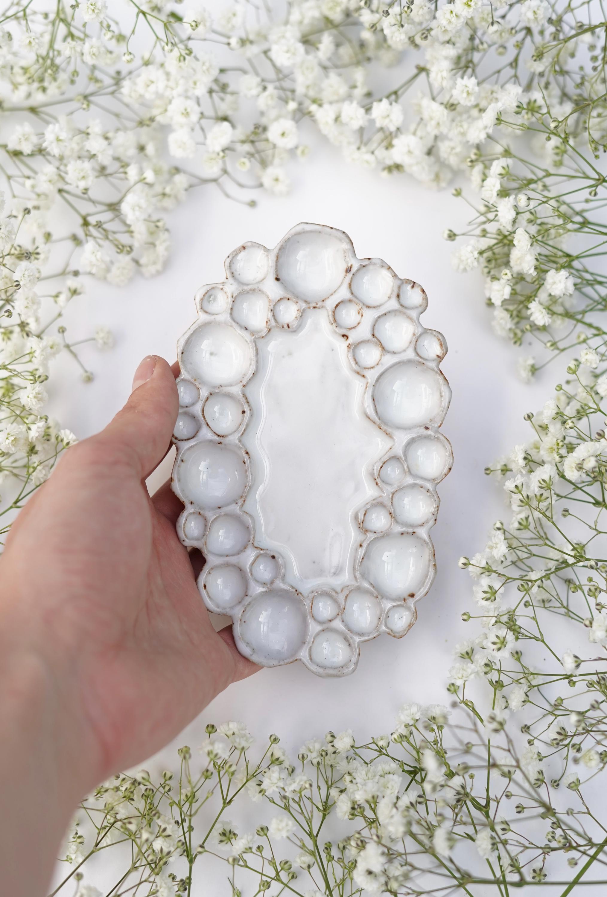 Hand holding mini ceramic oval bubble palette against white background with flowers