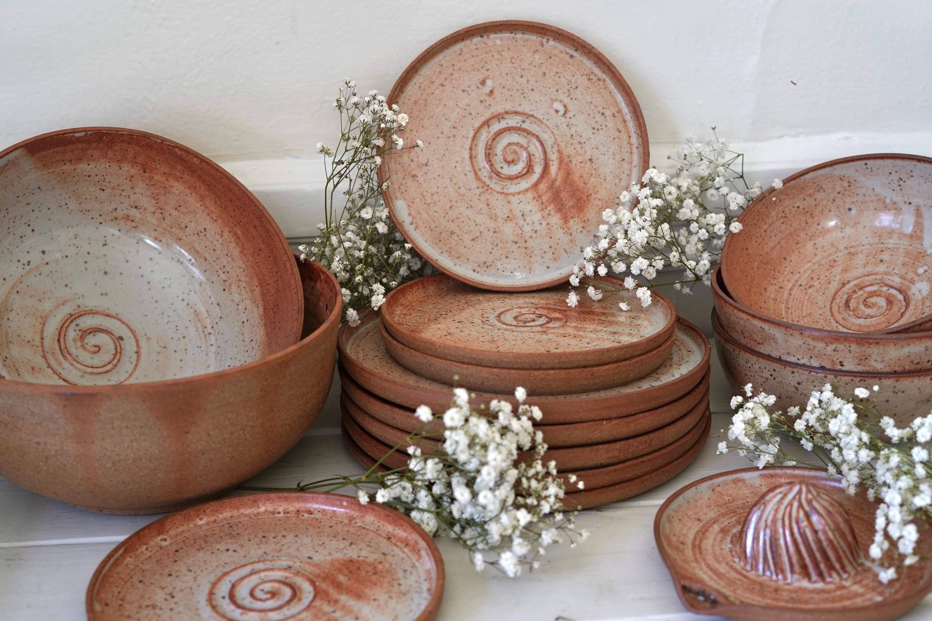 Set of orange ceramic plates and bowls with spiral patterns on a white surface with small white flowers.