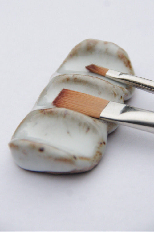 Ceramic brush rest with two paint brushes resting on it against white background 