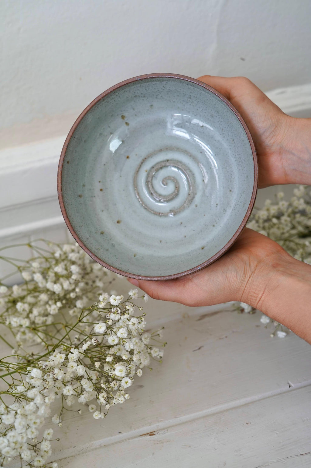 Hand holding a light blue ceramic bowl with a spiral design against a neutral background