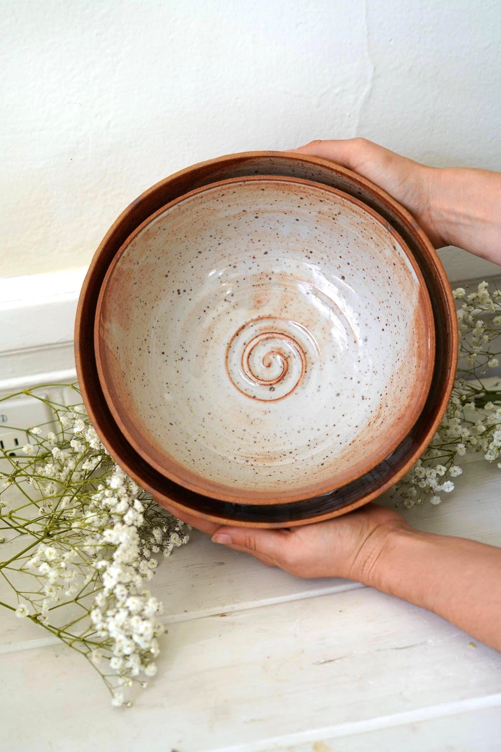 Hand holding two nesting orange ceramic bowls with a spiral design on a light background