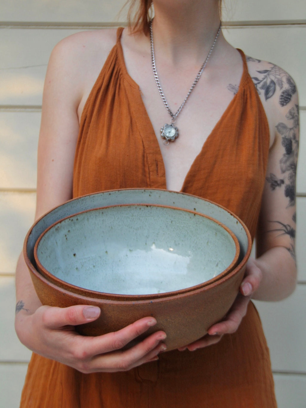 Person holding two large ceramic bowls with a neutral background