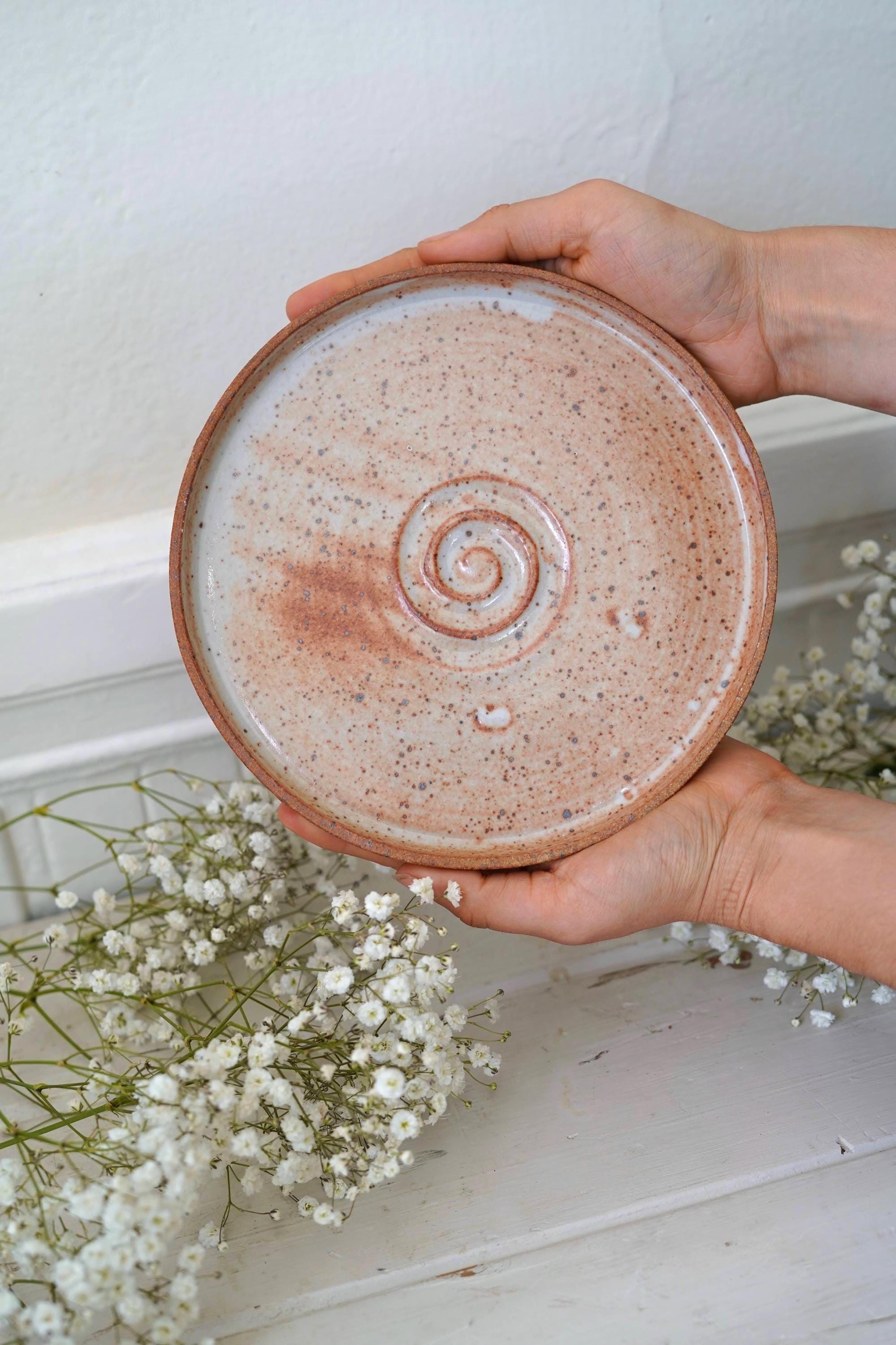 Hand holding an orange ceramic plate with a spiral design against a white background with flowers.