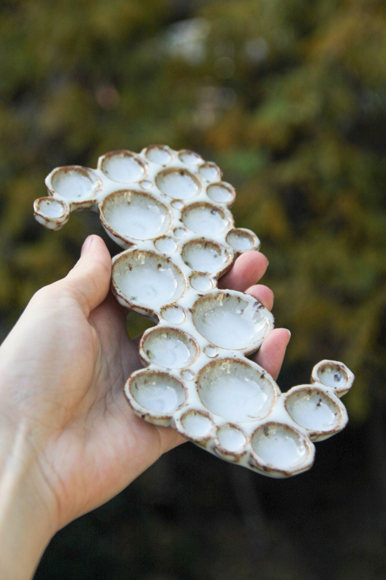 Hand holding large ceramic bubble palette from the side against green background 