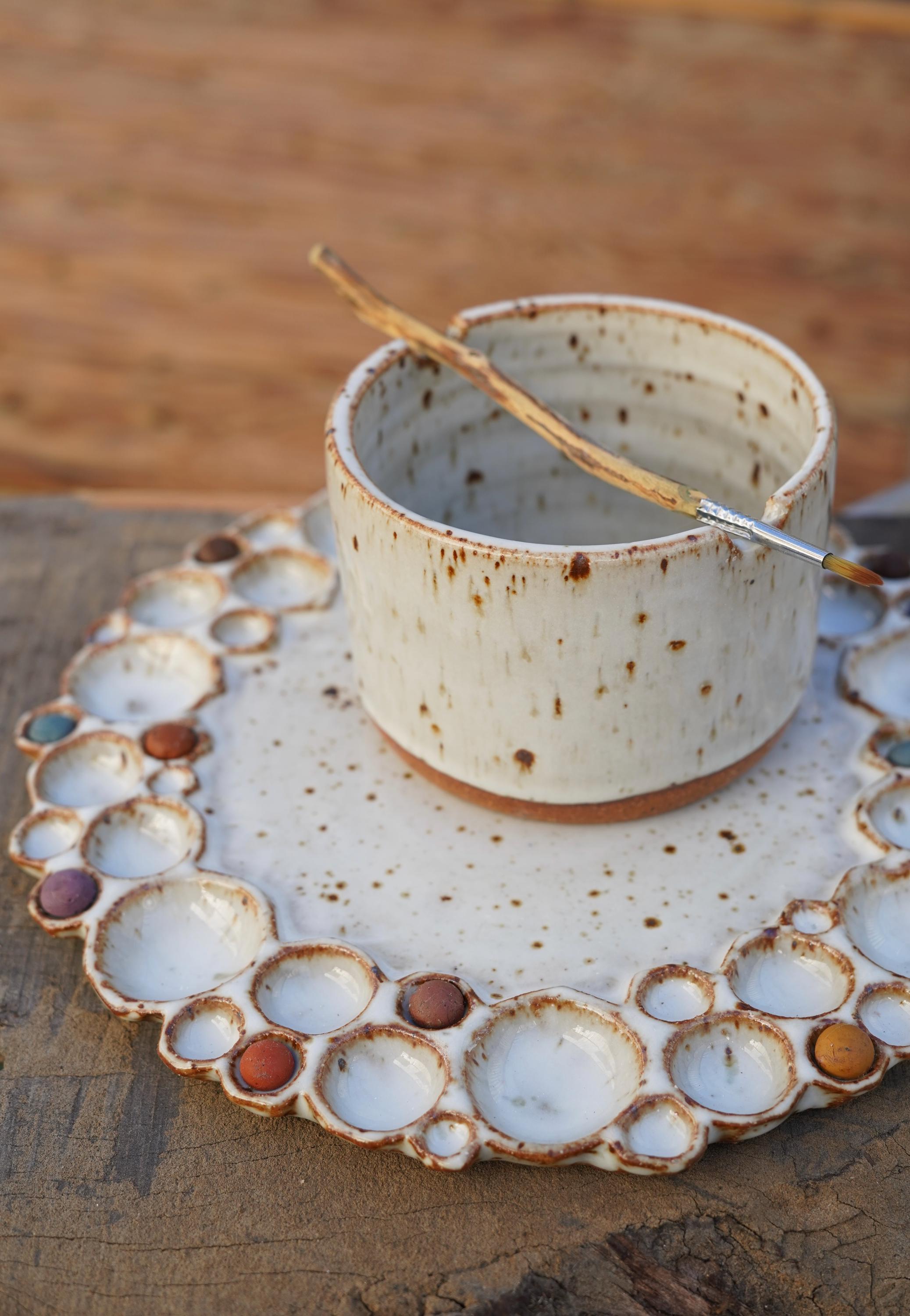 Ceramic watercolor cup with speckled white speckled glaze on a matching watercolor palette with paint 