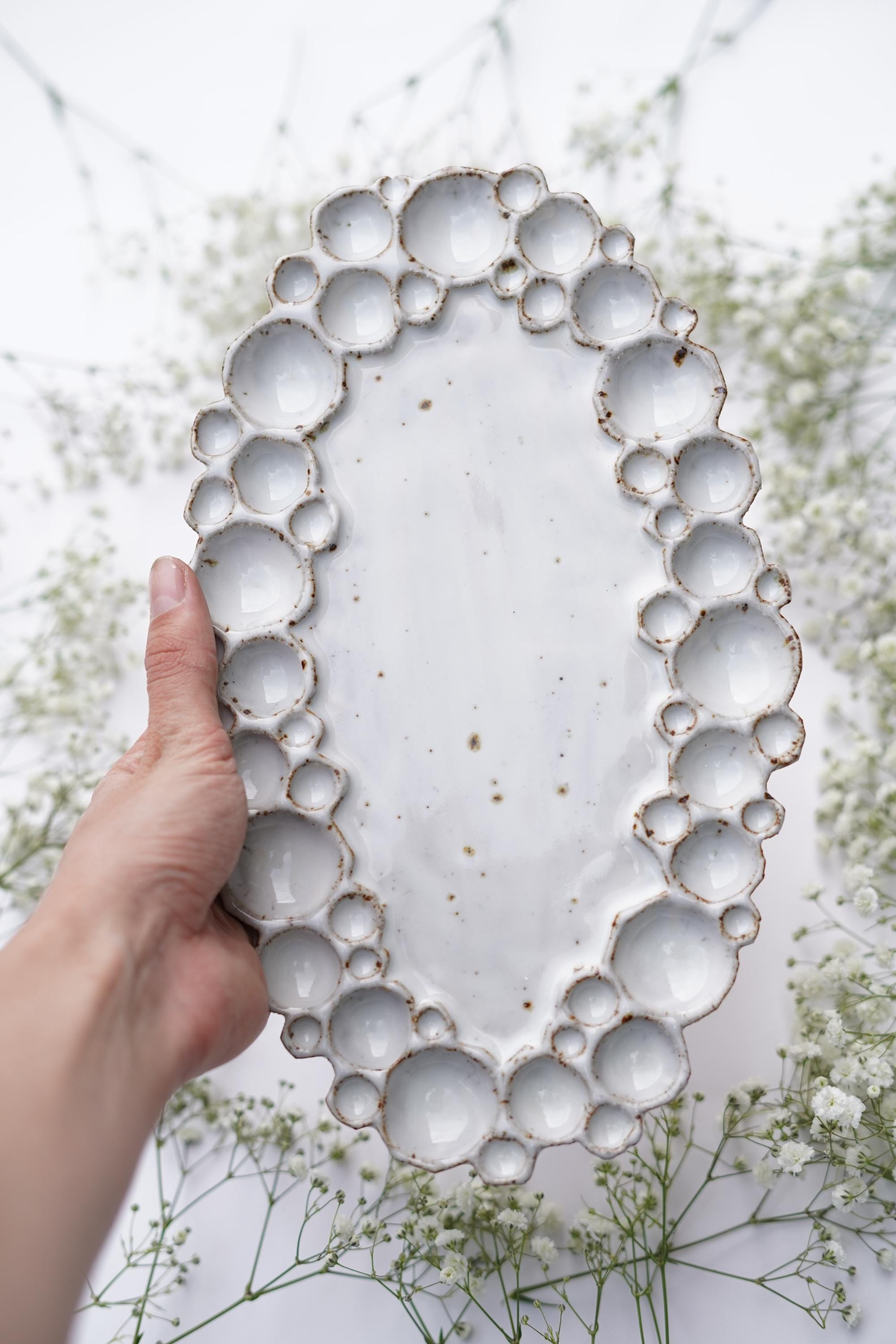 Hand holding large ceramic oval bubble palette agains white background with flowers 