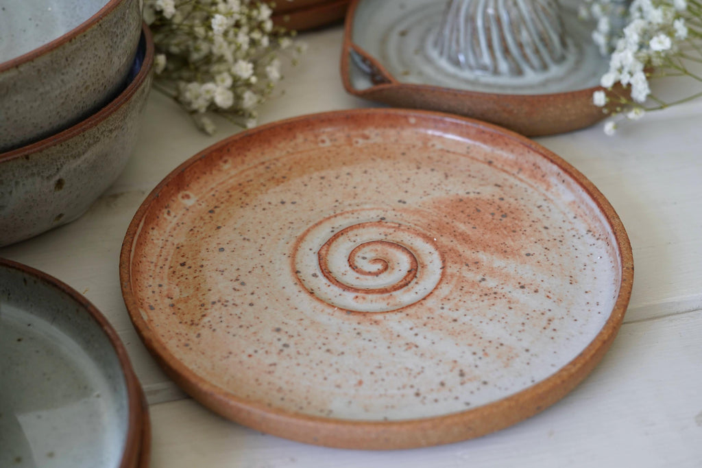 Orange ceramic plate with a spiral design on a white surface with other ceramic items.