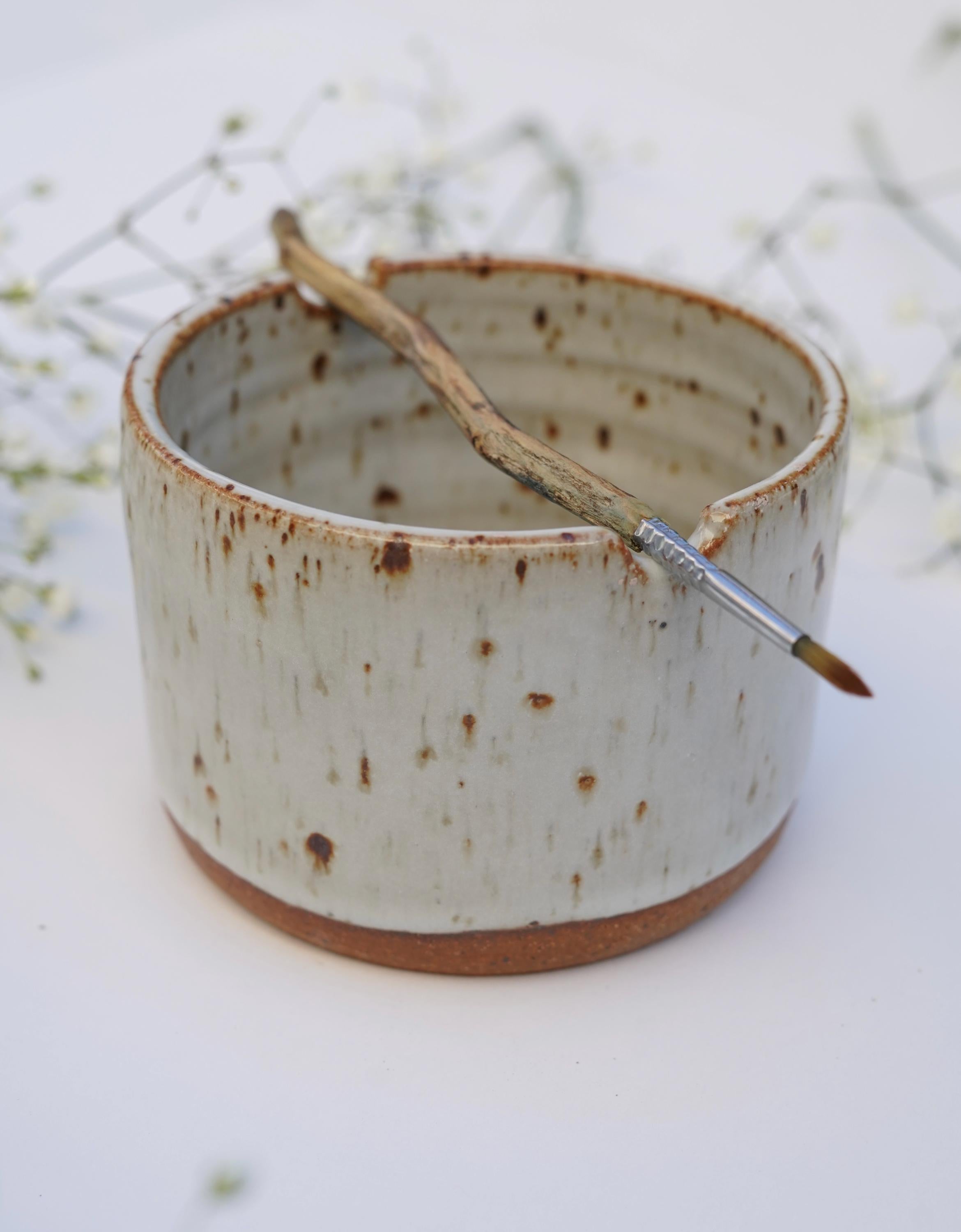 Ceramic watercolor cup with paint brush resting on the rim against white background 