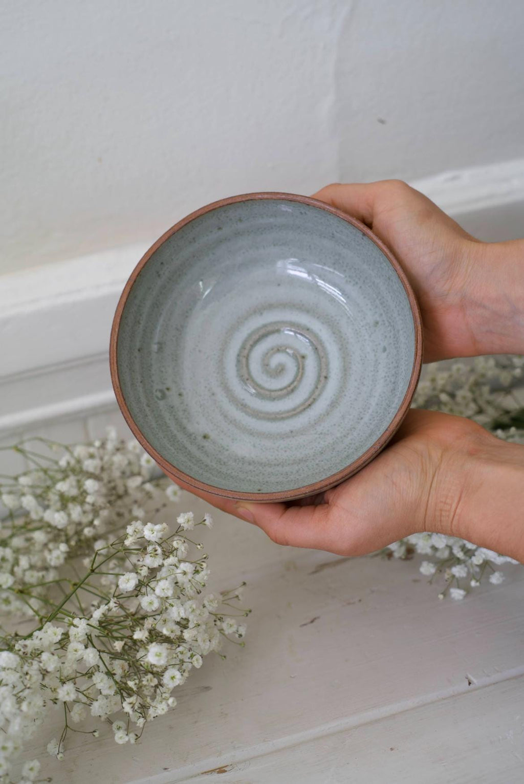Hand holding a ceramic bowl with a spiral pattern against a neutral background