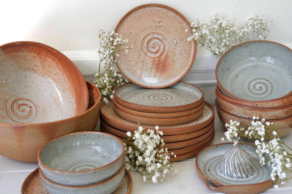 Collection of ceramic plates and bowls with spiral patterns on a white surface with small white flowers.