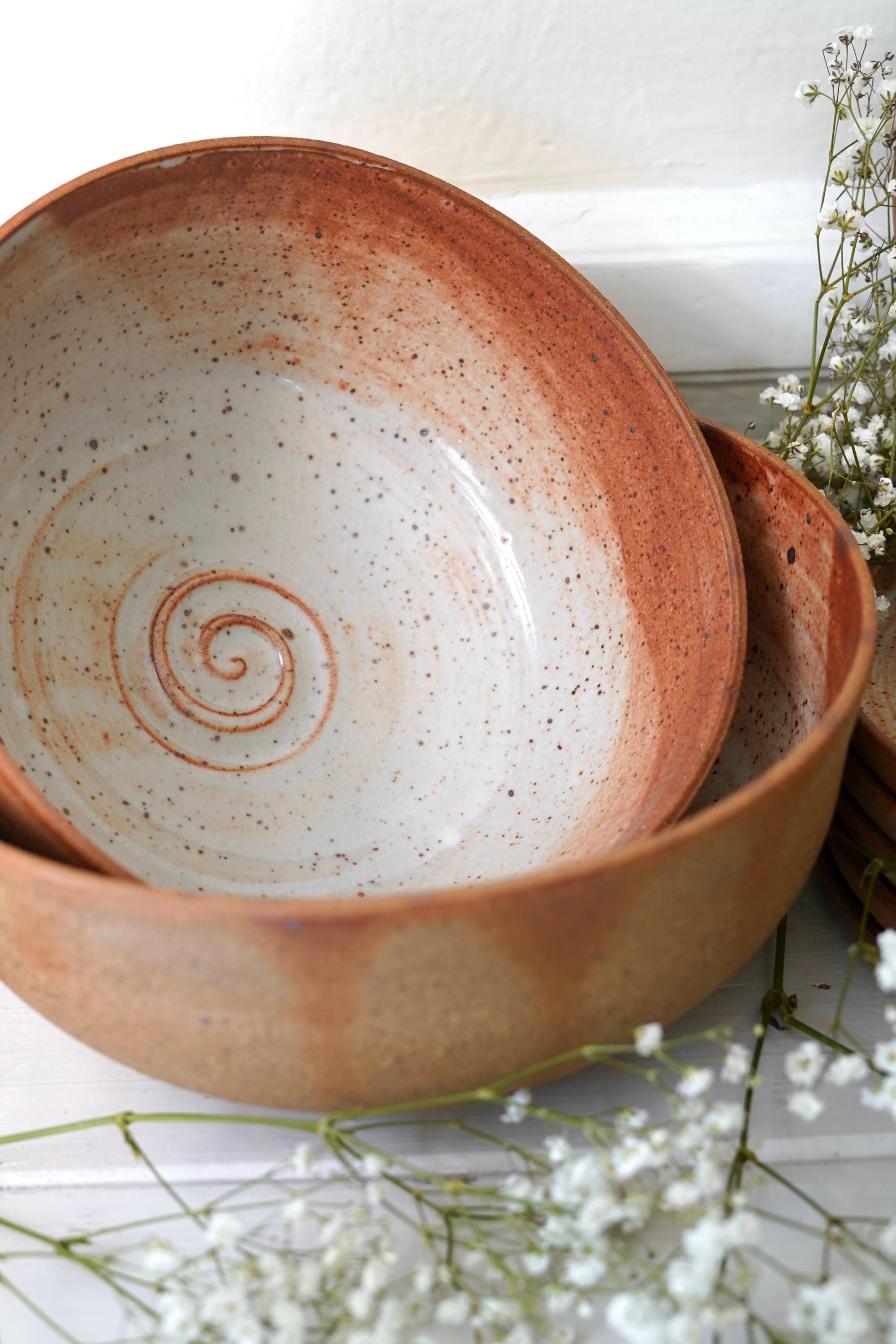 Two large ceramic serving bowls with spiral designs on a white surface with flowers.