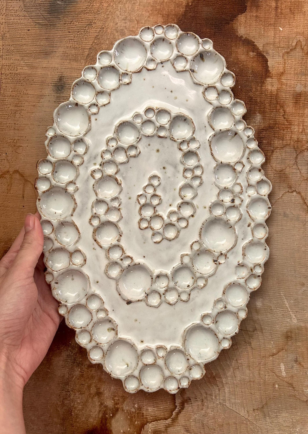 Hand holding ceramic spiral bubble palette against wood background 