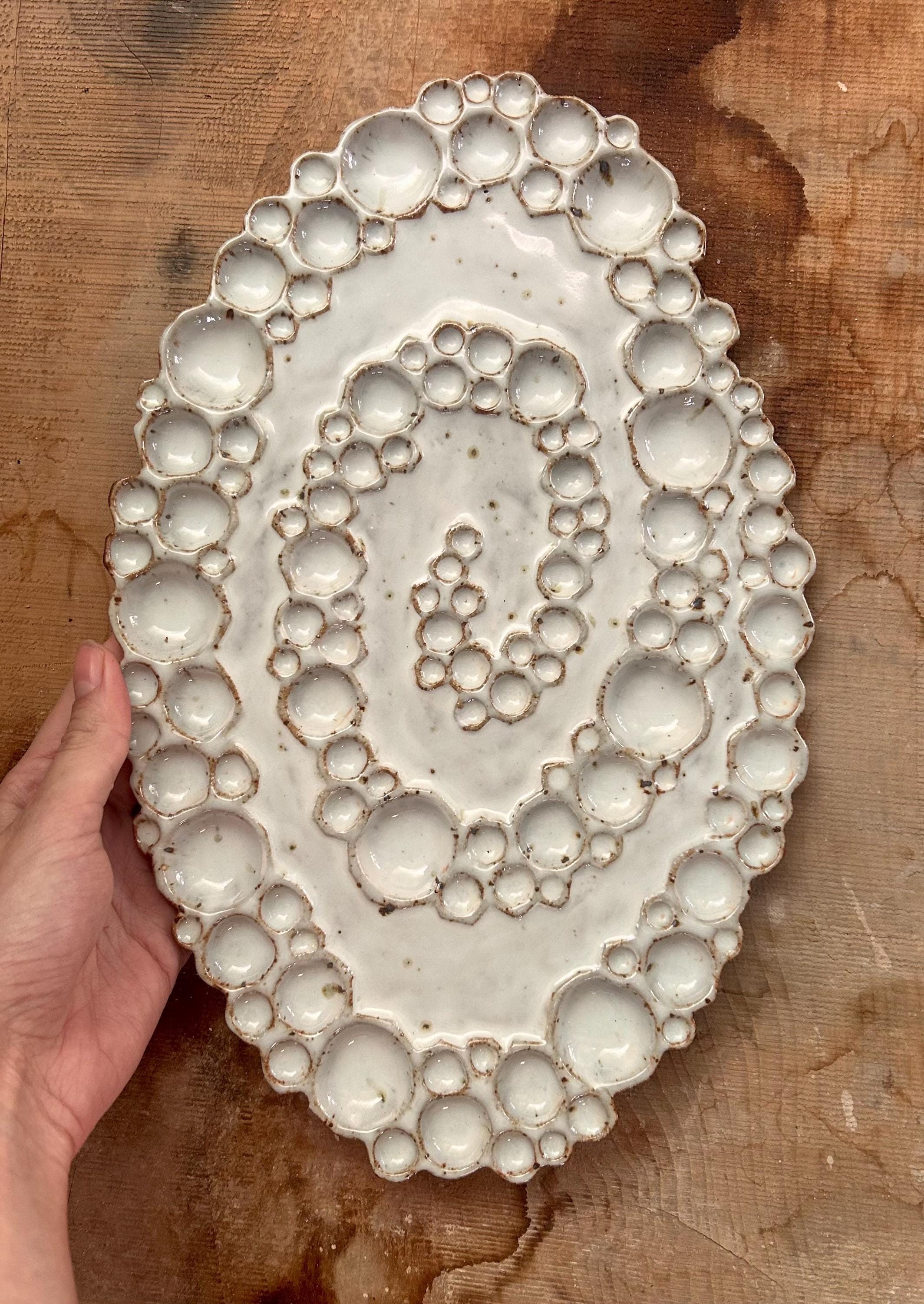 Hand holding ceramic spiral bubble palette against wood background 