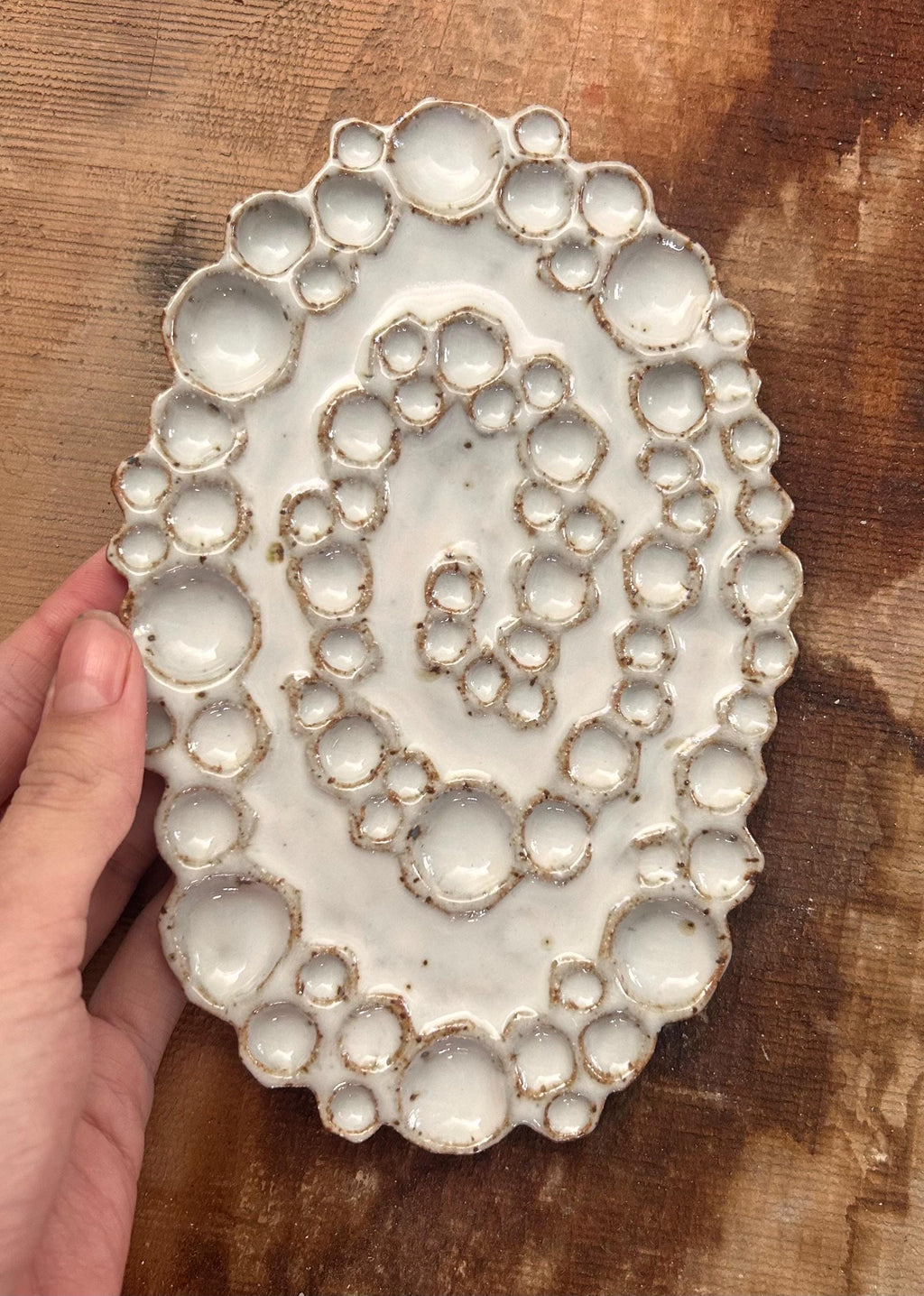 Hand holding mini ceramic spiral bubble palette against wood background 