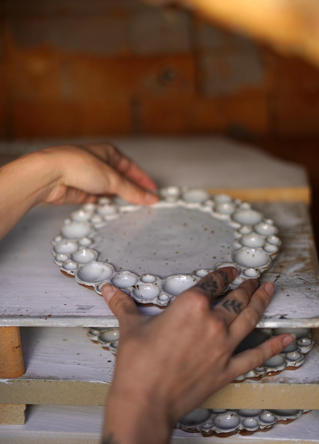 Two hands placing a round bubble palette on a kiln shelf