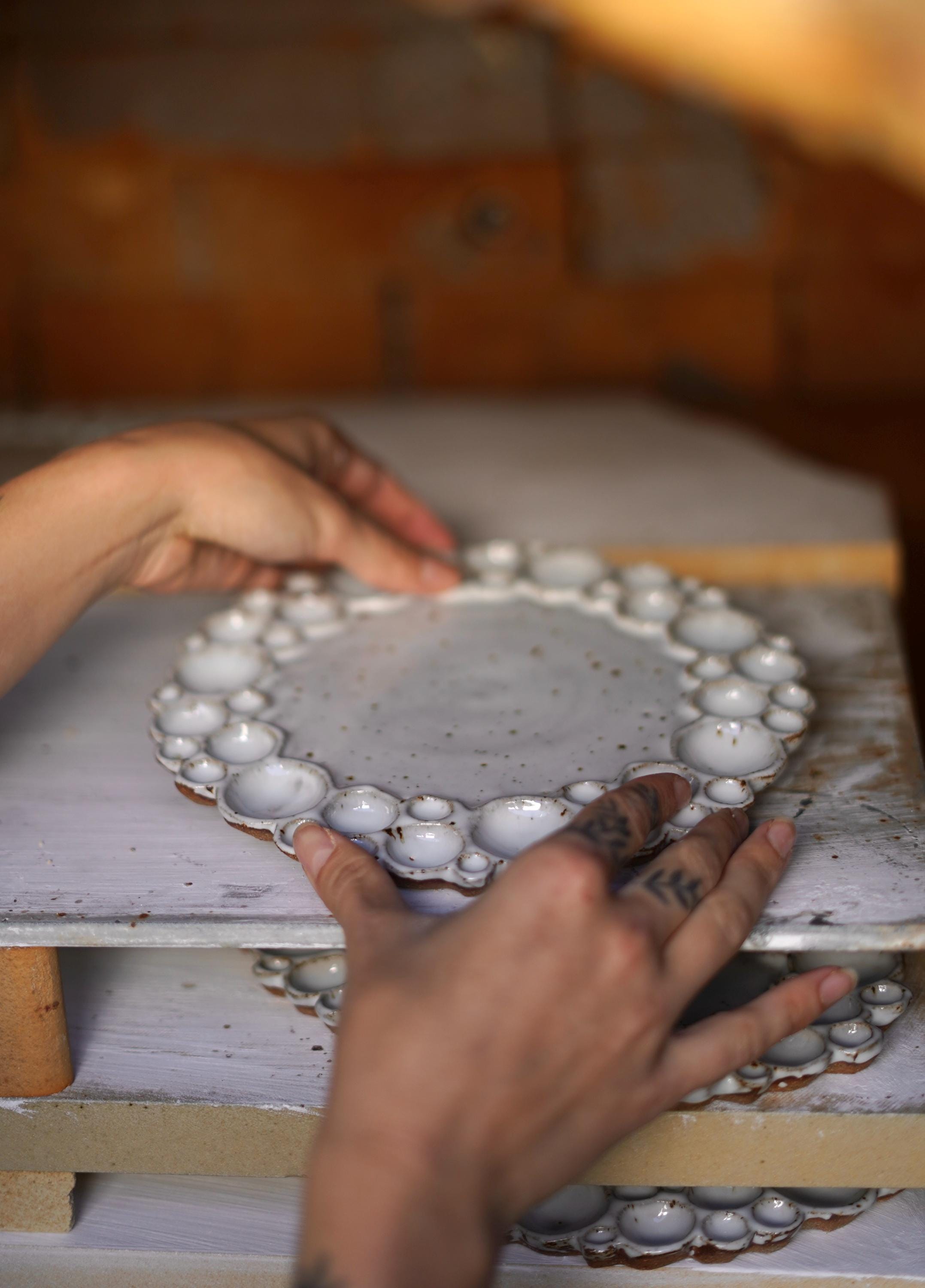 Two hands placing a round bubble palette on a kiln shelf