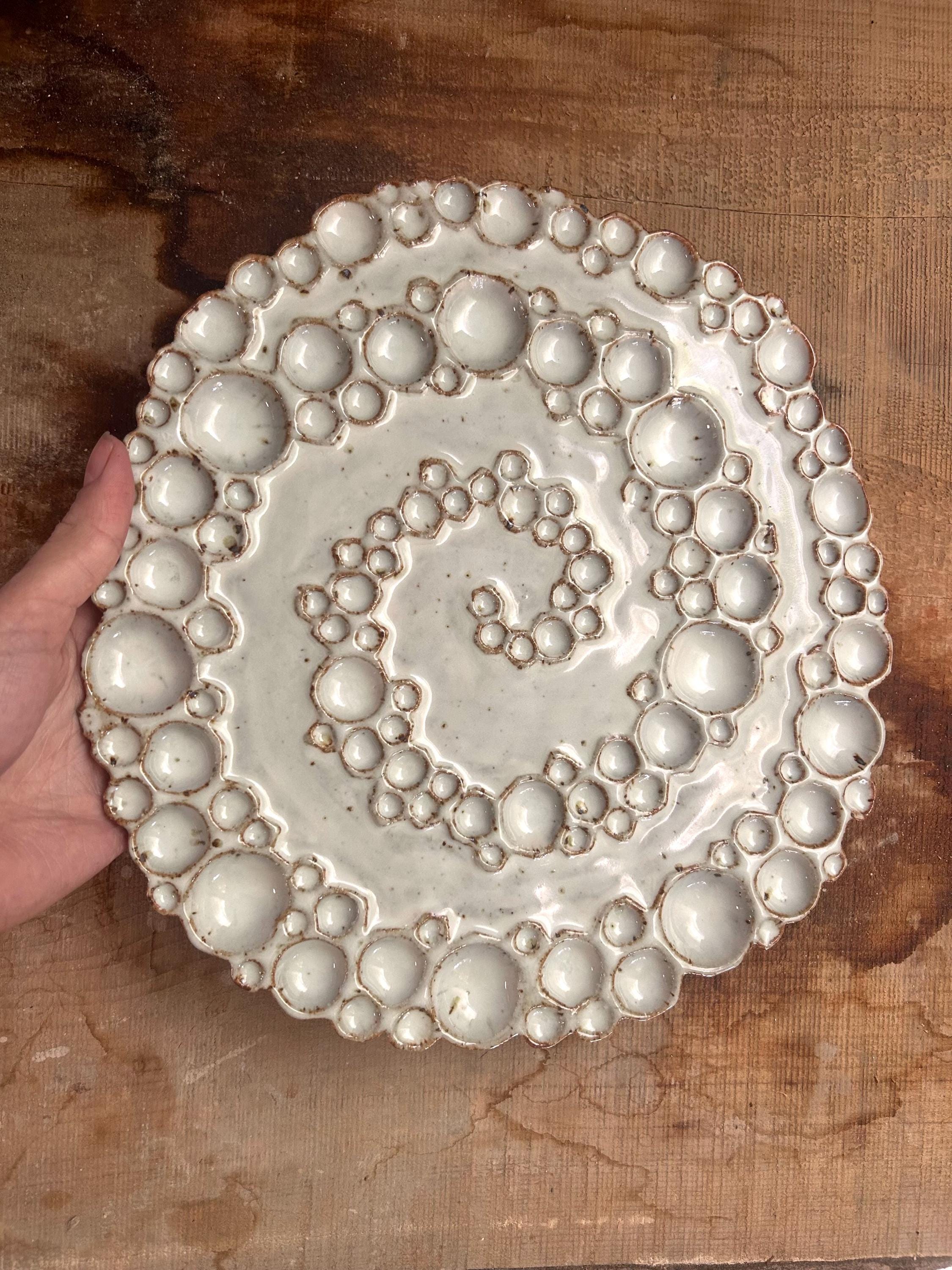 Hand holding large round ceramic spiral bubble palette on wooden surface 