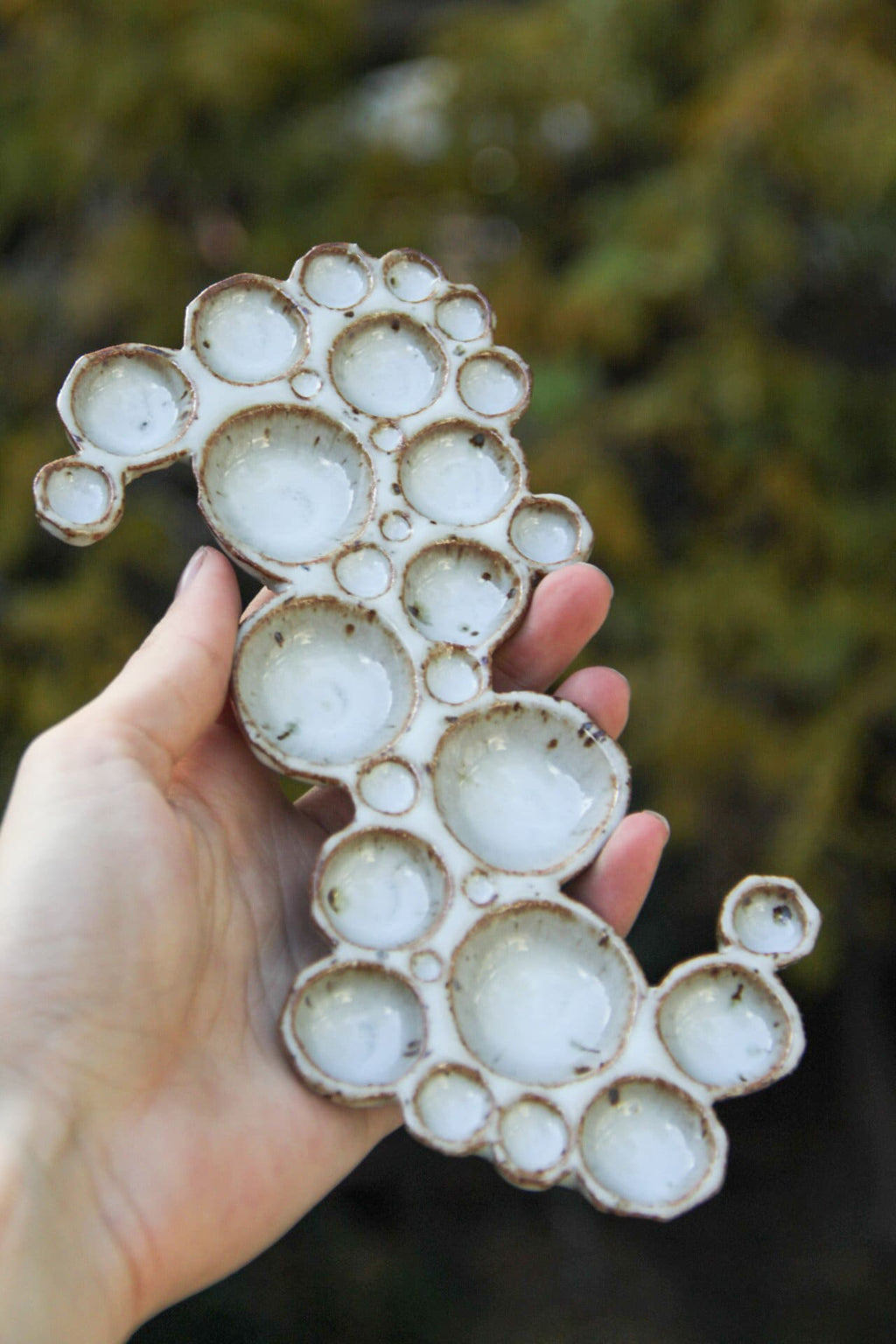 Hand holding large ceramic bubble palette against green background 