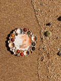 Round watercolor palette with wells with paint inside them on a sandy beach with shells 