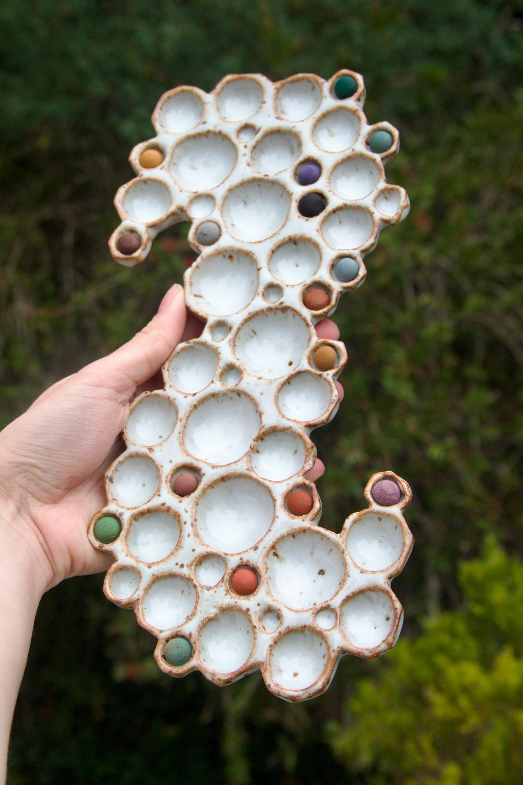 Hand holding x-large ceramic bubble palette with paint inside against green background 